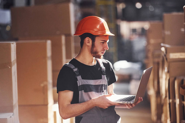 Storage worker in uniform and modern laptop in hands checks production. - Foto, Imagen