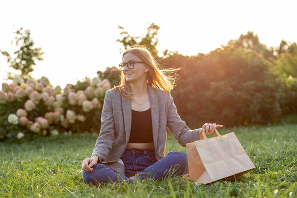 Голодна кавказька бізнесменка, студент або фрілансер з паперовими сумками, що сидять в парку, наказуючи забрати їжу. Відпочинок і перерва на роботі.. - Фото, зображення