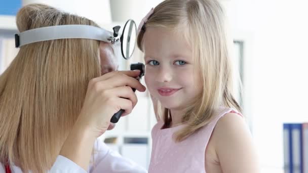 Entrée avec réflecteur frontal examinant petite fille oreille avec otoscope film 4k - Séquence, vidéo