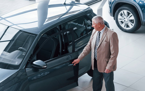 Aged man in formal wear walking in the automobile salon and looking for the car. - 写真・画像