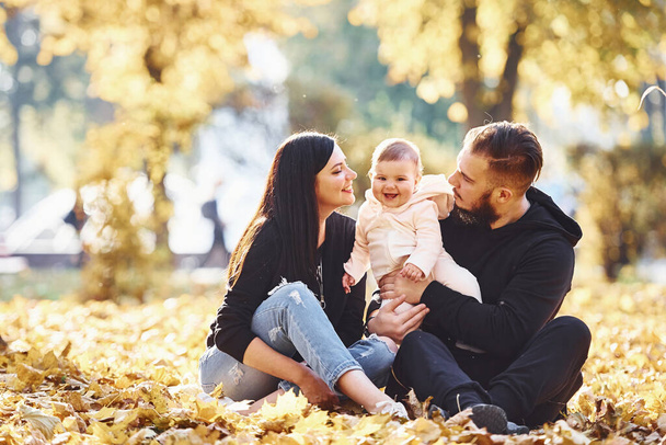 Sitting on the ground. Cheerful family having fun together with their child in beautiful autumn park. - Foto, Imagem