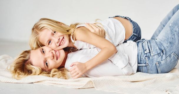 Mother with her daughter together is on the ground in the studio with white background. - Photo, image