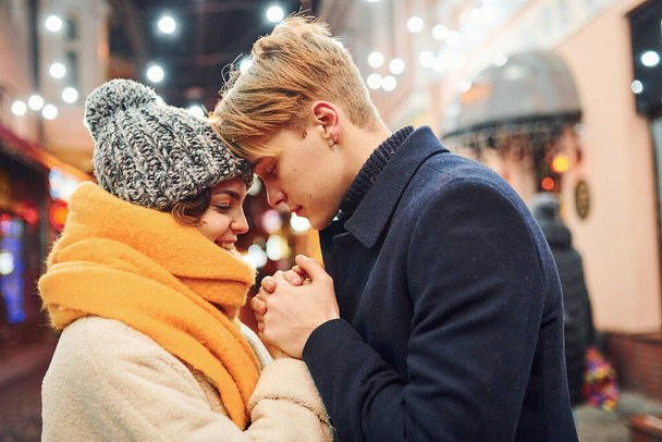 Closeness of the people. Happy young couple in warm clothes is on christmas decorated street together. - Foto, immagini