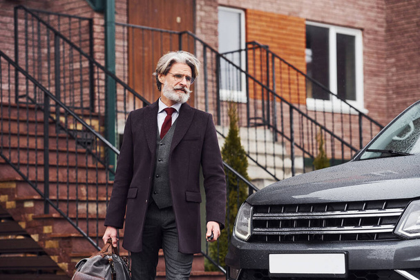 Fashionable senior man with gray hair and beard is outdoors on the street near his car. - Foto, Imagem