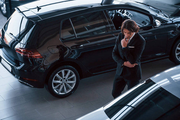 Portrait of handsome young businessman in black suit and tie indoors near modern car. - Photo, image
