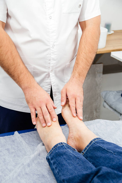 an osteopath touches a womans feet with his fingers, conducts a therapeutic test on a massage couch - Φωτογραφία, εικόνα