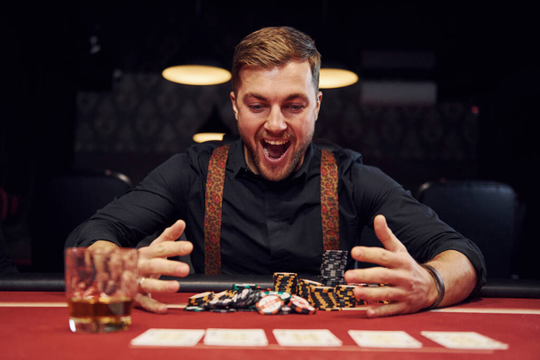 Happy elegant young man sits in casino and celebrate his victory in poker game. - Fotografie, Obrázek