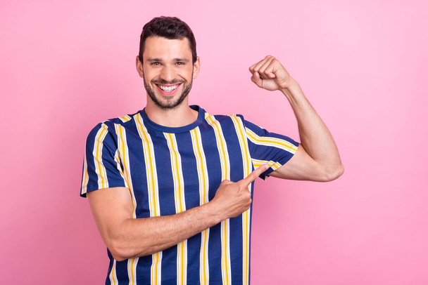 Фотопортрет мужчина улыбается указывая пальцем сильные бицепсы изолированные пастельно-розовый цвет фона - Фото, изображение
