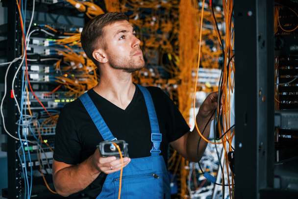 Young man in uniform have a job with internet equipment and wires in server room. - Foto, immagini