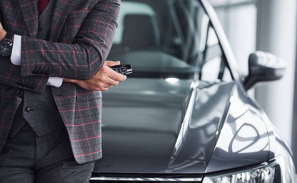 Man in modern formal clothes stands against black car with keys in hand. - Foto, immagini