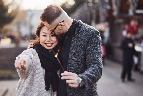 With sparklers in hands. Happy multiracial couple together outdoors in the city. - 写真・画像