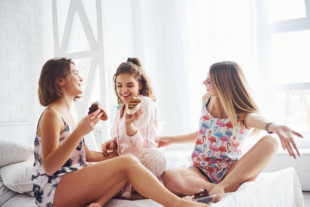 Eating sweets together. Happy female friends having good time at pajama party in the bedroom. - Foto, immagini