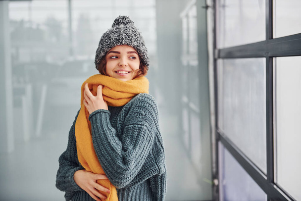 Beautiful cheerful girl in yellow scarf and in warm clothes standing indoors. - Foto, imagen