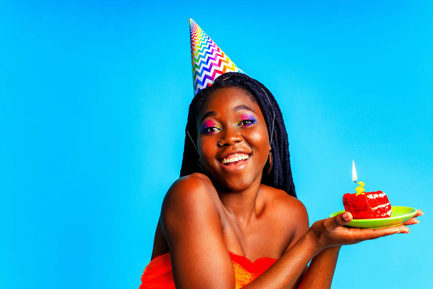 beautiful afro woman with georgeus makeup wear birthday hat and hold cake in blue studio - Fotó, kép