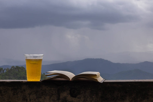 Un vaso de cerveza colocado al lado de la Biblia en el balcón sobre una hermosa vista de la temporada de lluvias. Las enseñanzas de Dios en la Biblia advierten que cuando bebes mucho alcohol no puedes controlarte.. - Foto, imagen