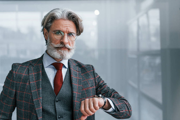 Senior businessman in suit and tie with gray hair and beard standing and checks time. - Foto, Imagem