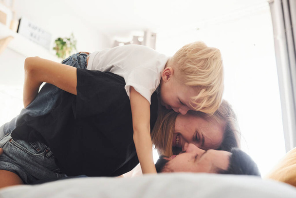 Young married couple with their young son lying down on bed and have fun together in bedroom at daytime. - Fotografie, Obrázek