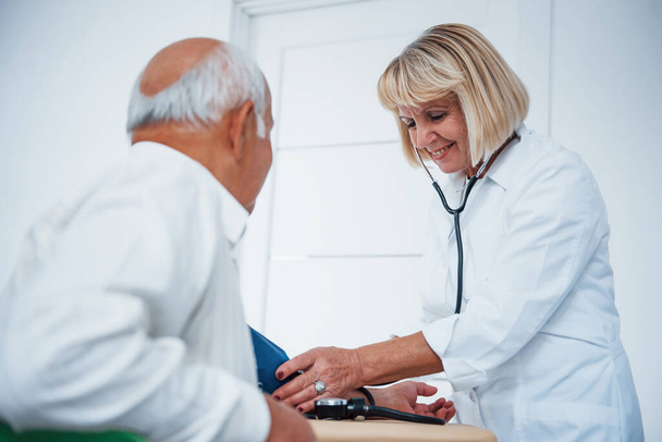 Female doctor uses tonometer to make blood pressure measuring to senior man. - Fotoğraf, Görsel