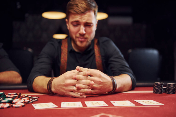 Elegant young man sits in casino and feels bad because loses poker game. - Foto, Imagen