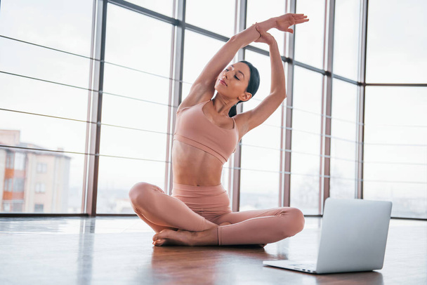 Brunette with slim body type doing exercises on the floor and using laptop. - Φωτογραφία, εικόνα