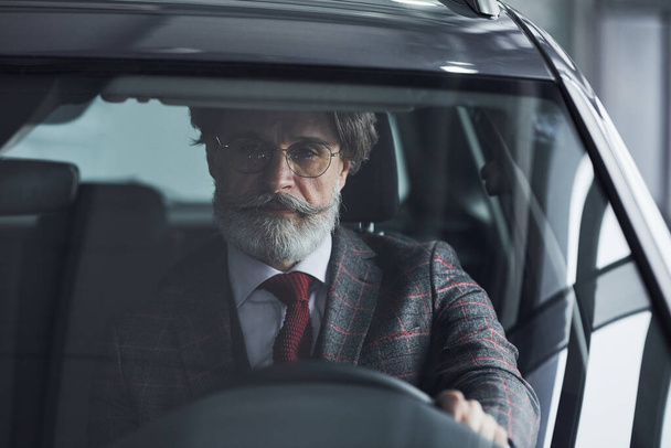 Hombre de negocios senior en traje y corbata con pelo gris y barba conduciendo el coche. - Foto, imagen