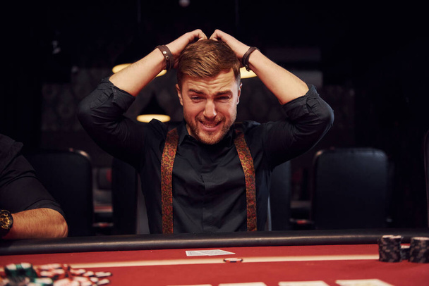 Elegant young man sits in casino and feels bad because loses poker game. - Fotografie, Obrázek