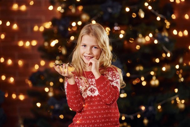 Cute little girl in near christmas tree indoors celebrating new year. - Fotó, kép