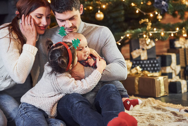 Kaunis valkoihoinen pari juhlii joulua sisätiloissa pienen poikansa ja tyttärensä kanssa.. - Valokuva, kuva