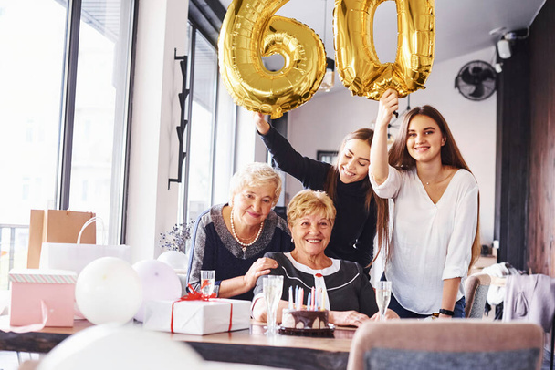 Balloons with number 60. Senior woman with family and friends celebrating a birthday indoors. - Foto, afbeelding