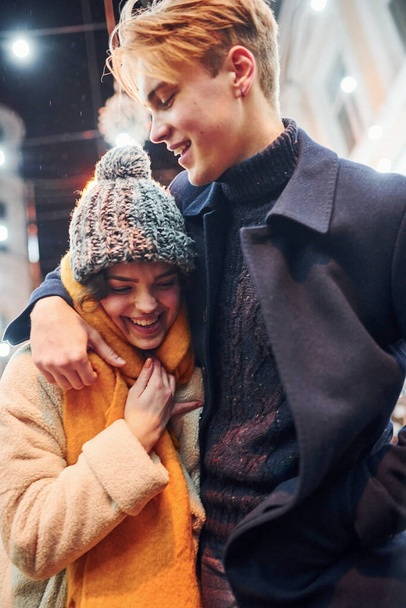 Positive young couple in warm clothes embracing each other on christmas decorated street. - Foto, immagini