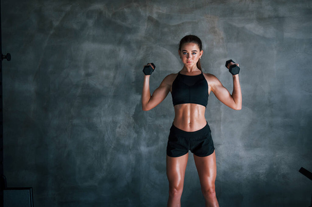 Young fitness woman is in the gym near wall with dumbbells in hands. - Foto, Imagen