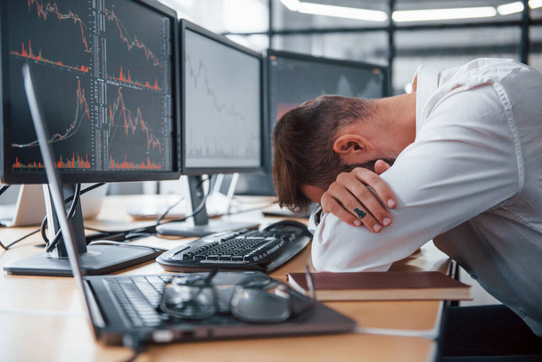 Tired businessman sleeping on the workplace by leaning on the table with multiple screens on it. Stock information on displays. - Foto, imagen