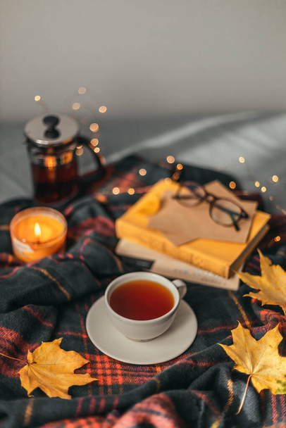 Ζεστό καρό μαντήλι, ένα φλιτζάνι αρωματικό μαύρο τσάι και φύλλα σφενδάμου στο κρεβάτι. Άνετο φθινόπωρο. - Φωτογραφία, εικόνα