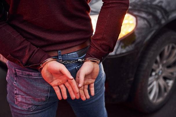 Woman standing in handcuffs near modern automobile outdoors. - 写真・画像