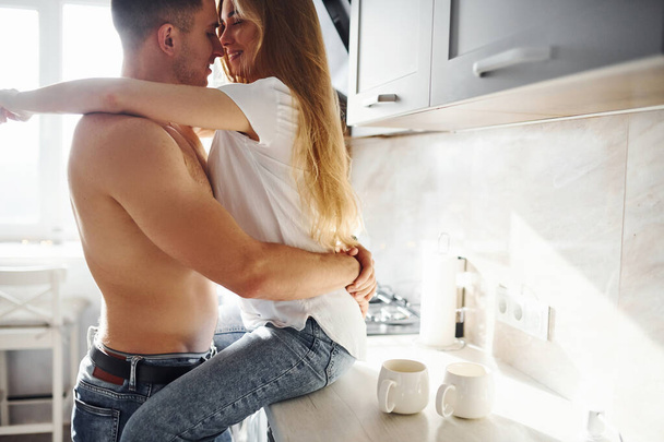 Young couple embracing and kissing each other on the kitchen. - Zdjęcie, obraz