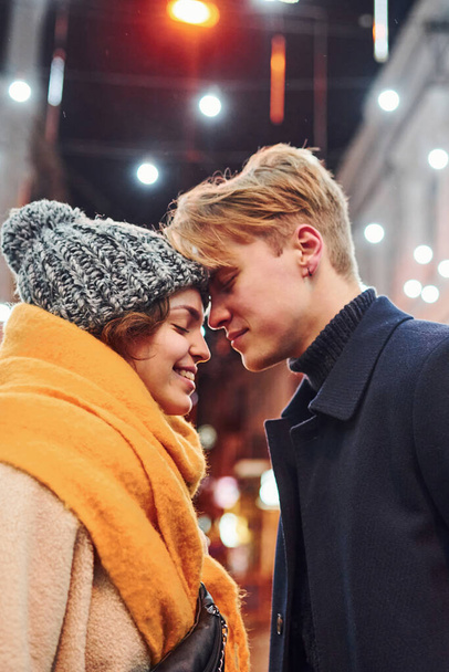Cute couple in warm clothes is on christmas decorated street smiling and have fun. - 写真・画像