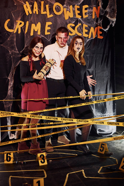 Standing against crime scene wall. Friends is on the thematic halloween party in scary makeup and costumes. - Fotografie, Obrázek