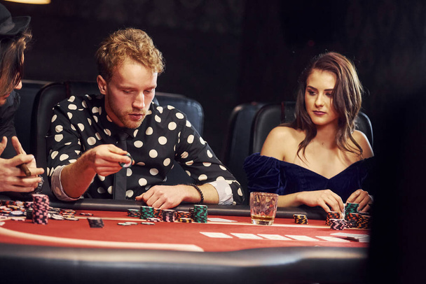 With glasses of drink. Group of elegant young people that playing poker in casino together. - Foto, Bild