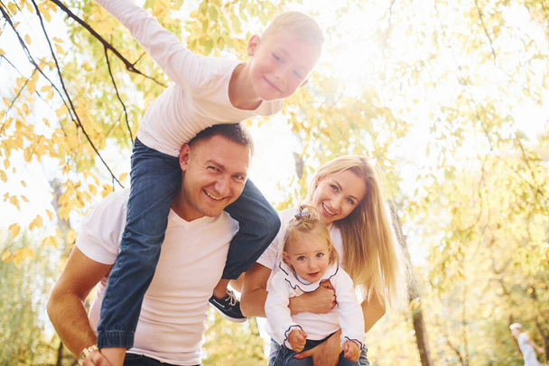 Mother and dad holds kids at shoulders and in hands. Cheerful young family have a walk in an autumn park together. - Foto, Imagem