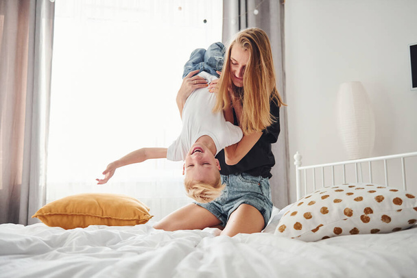 Mother playing and have fun with her son in bedroom at daytime. - Foto, afbeelding