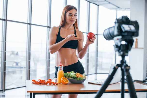 Női vlogger sportos test áll beltérben közelében asztal egészséges étel. - Fotó, kép