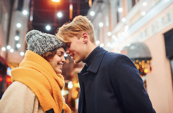 Cute couple in warm clothes is on christmas decorated street smiling and have fun. - Valokuva, kuva