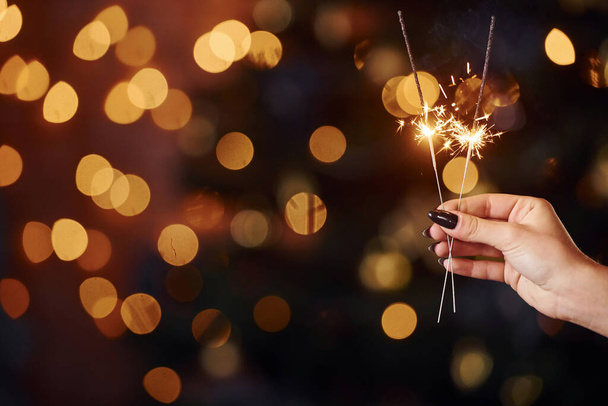 Close up view of woman's hand with sparkler indoors at christmas holidays. - Foto, imagen