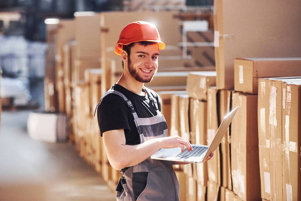 Storage worker in uniform and modern laptop in hands checks production. - Photo, Image