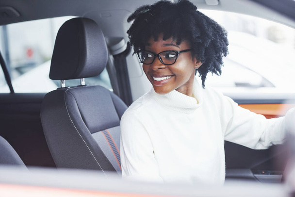 Young african american woman sits inside of new modern car. - Fotografie, Obrázek