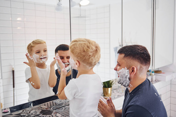 Father with his son is in the bathroom have fun by using shaving gel and looking in the mirror. - Valokuva, kuva