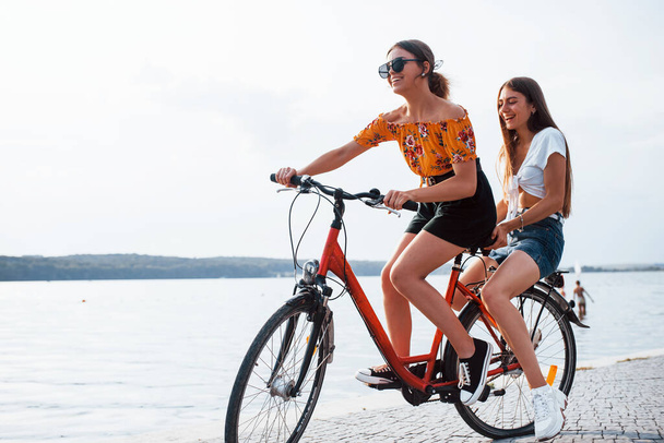 Duas amigas na bicicleta se divertem na praia perto do lago. - Foto, Imagem