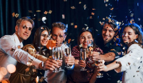 Knocking glasses. Group of cheerful friends celebrating new year indoors with drinks in hands. - Photo, image