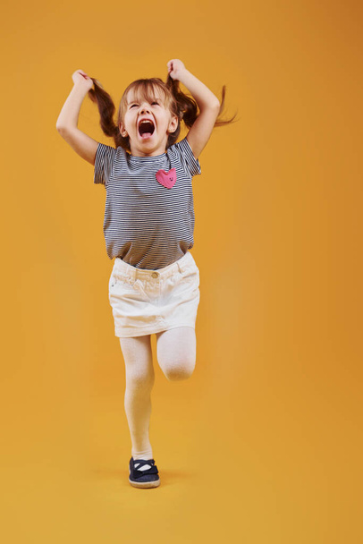 Cute little girl in casual clothes have fun in the studio against yellow background. - 写真・画像