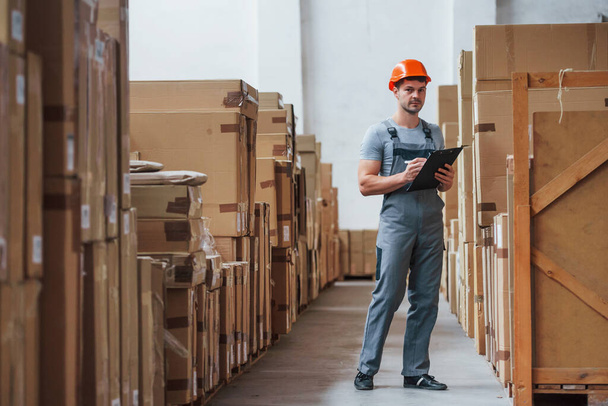 Young male worker in uniform is in the warehouse with notepad and pen. - 写真・画像
